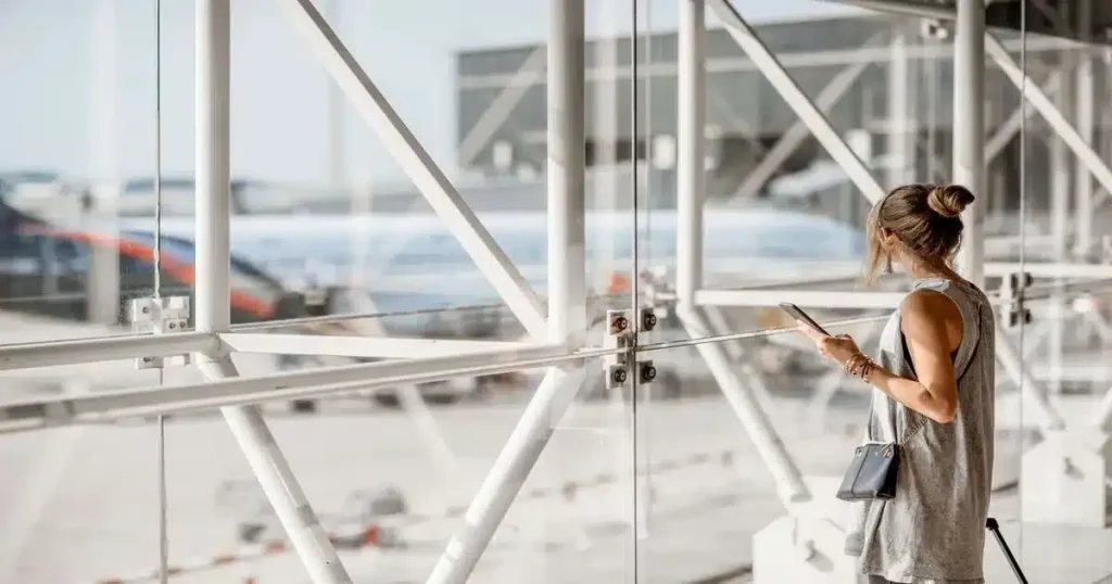 Une femme qui se situe dans un hall, regardant les avions sur le tarmac.