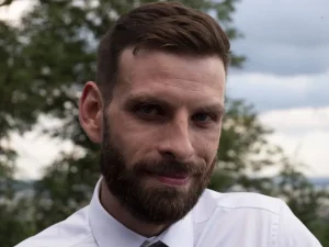 Une personne souriante regardant l'objectif. En arrière plan des branches d'arbres