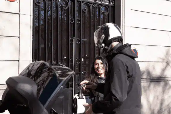 un chauffeur qui prend le sac à mon. une femme souriante devant une porte ornée d'une grille en fer forgé.