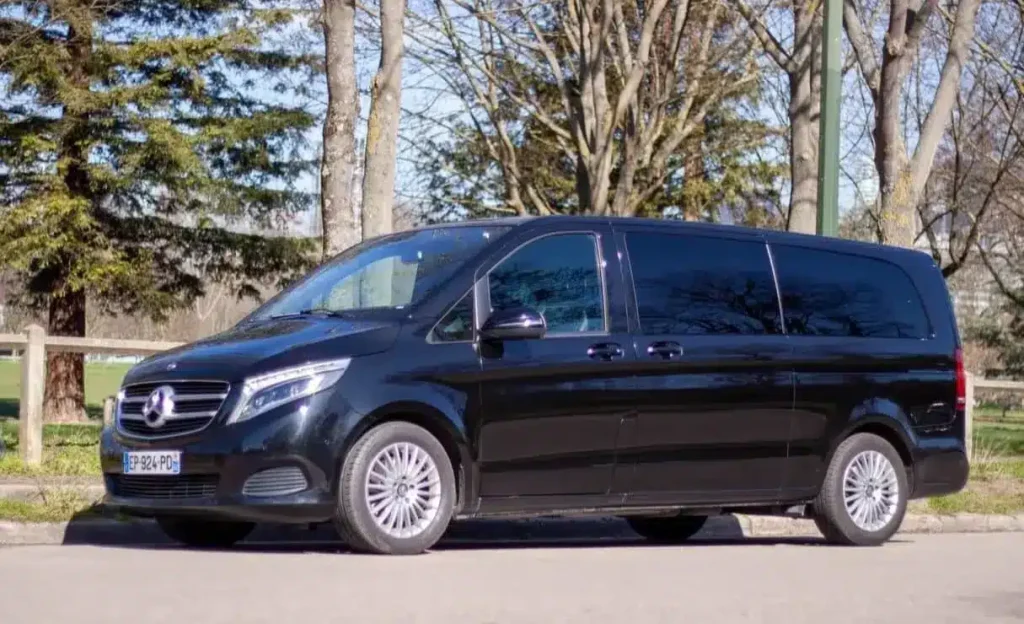 Un van mercedes de couleur noir. Le van est au milieu d'un bois