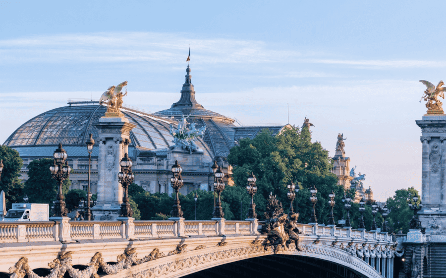 Vue panoramique du Pont Alexandre III à Paris avec le Grand Palais en arrière-plan à l'aube, orné de ses statues dorées emblématiques.